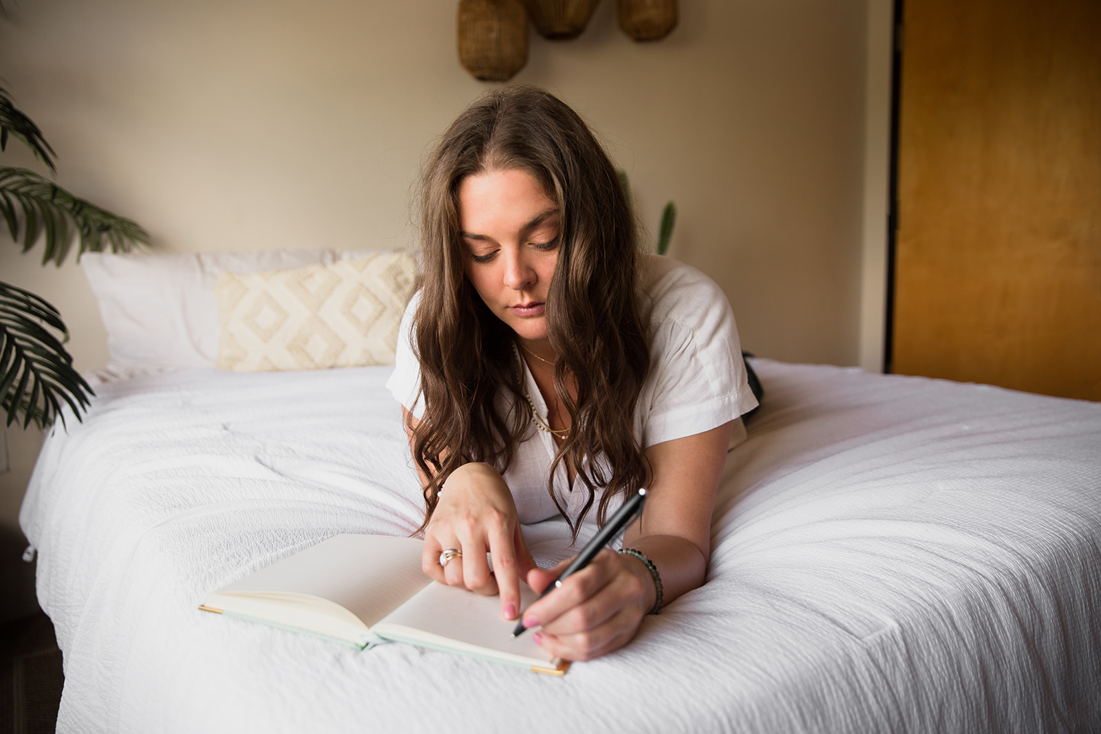 Heather Flynn journaling in a notebook while resting on a bed in a calm, softly lit room